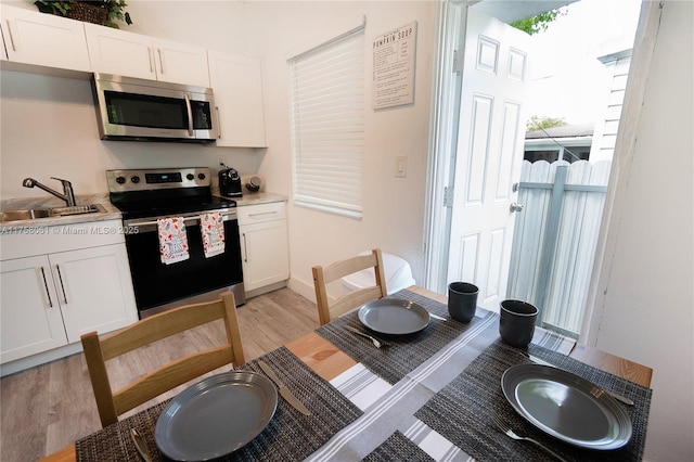 kitchen featuring appliances with stainless steel finishes, white cabinetry, light wood-style floors, and a sink