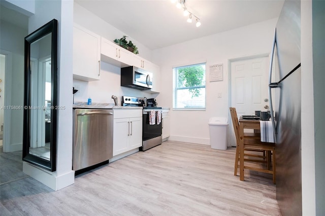 kitchen with light wood finished floors, appliances with stainless steel finishes, white cabinetry, and baseboards
