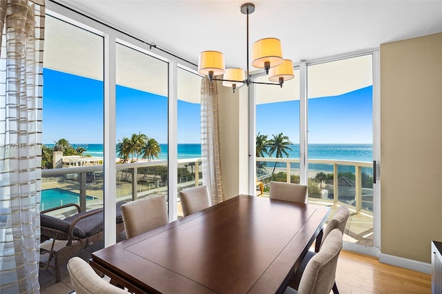 dining space featuring wood finished floors, a water view, an inviting chandelier, and expansive windows