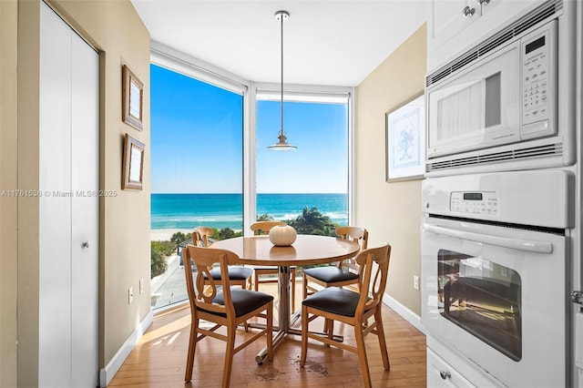 dining area featuring baseboards, a water view, expansive windows, light wood-style floors, and a glass covered fireplace