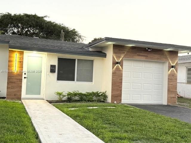 view of front of house with a shingled roof, a front yard, stucco siding, a garage, and driveway