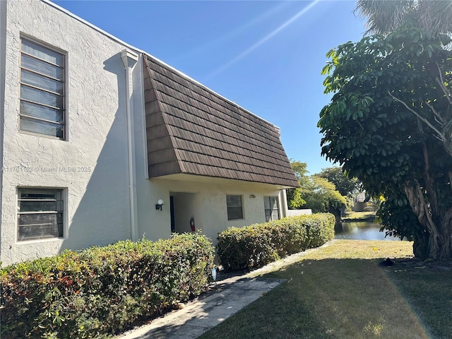 view of side of property featuring a lawn, a water view, and stucco siding