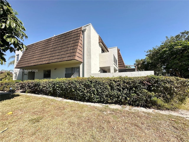 view of side of property featuring stucco siding and mansard roof