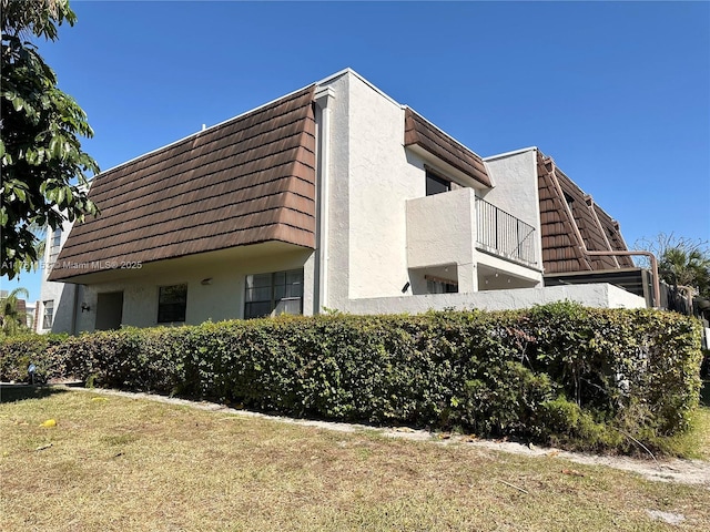 view of side of property featuring stucco siding and mansard roof