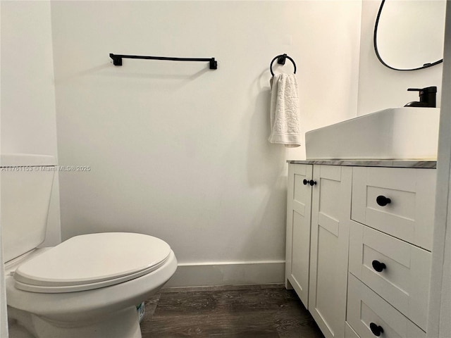 half bath featuring toilet, vanity, baseboards, and wood finished floors