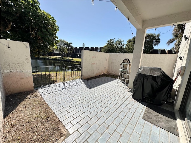 view of patio featuring grilling area, a water view, and fence