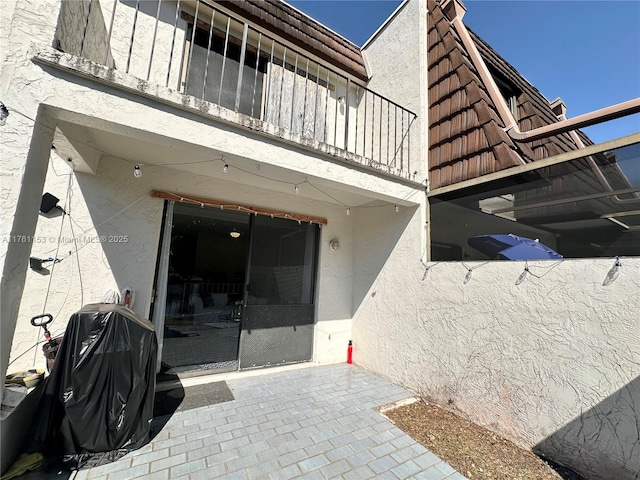 view of exterior entry featuring stucco siding, a patio, a balcony, and a tiled roof