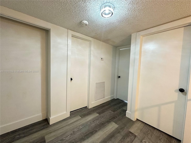 unfurnished bedroom with dark wood finished floors, visible vents, a textured ceiling, and baseboards