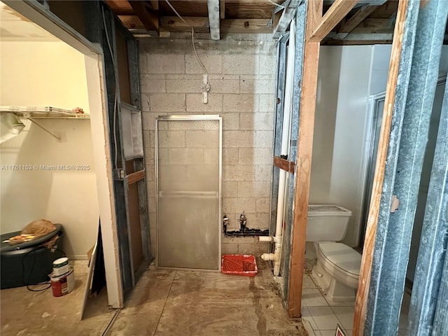 bathroom featuring toilet and concrete block wall