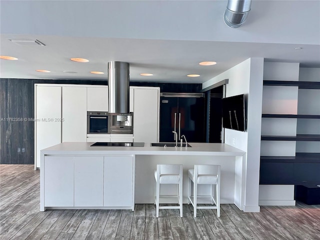 kitchen with built in refrigerator, stainless steel oven, a peninsula, wood finished floors, and modern cabinets