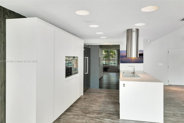 kitchen with light countertops, wood finished floors, modern cabinets, a sink, and white cabinetry