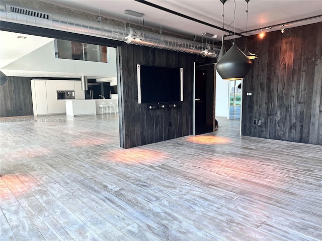 empty room with visible vents, wood finished floors, rail lighting, and wood walls