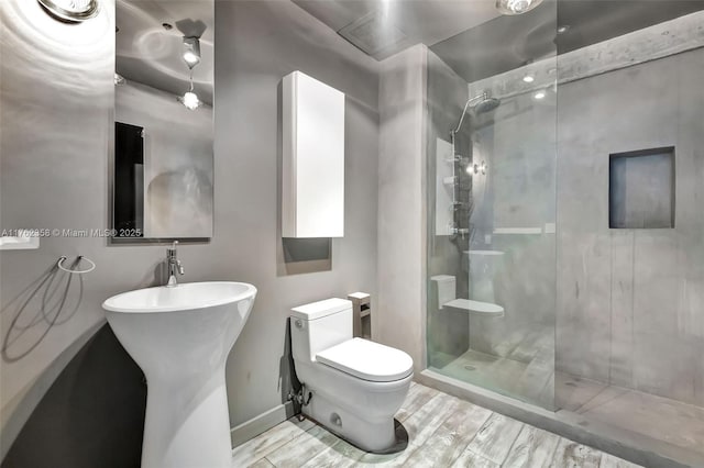 bathroom featuring walk in shower, baseboards, a sink, and toilet