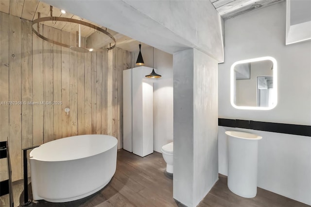 bathroom with a freestanding bath, toilet, walk in shower, wood finished floors, and wooden walls