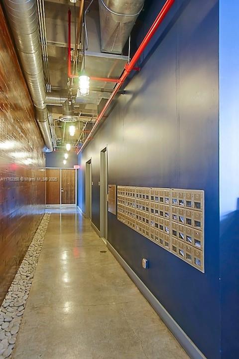 hallway featuring finished concrete flooring, mail area, and baseboards