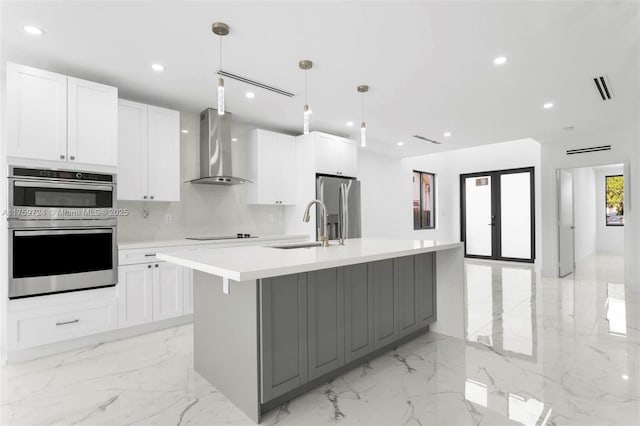 kitchen featuring marble finish floor, a sink, appliances with stainless steel finishes, wall chimney range hood, and a large island with sink