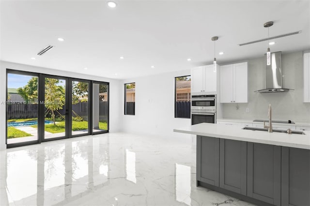 kitchen featuring visible vents, marble finish floor, stainless steel double oven, wall chimney exhaust hood, and light countertops