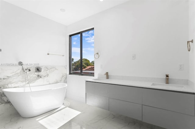 full bathroom featuring a freestanding tub, marble finish floor, a sink, tile walls, and wainscoting