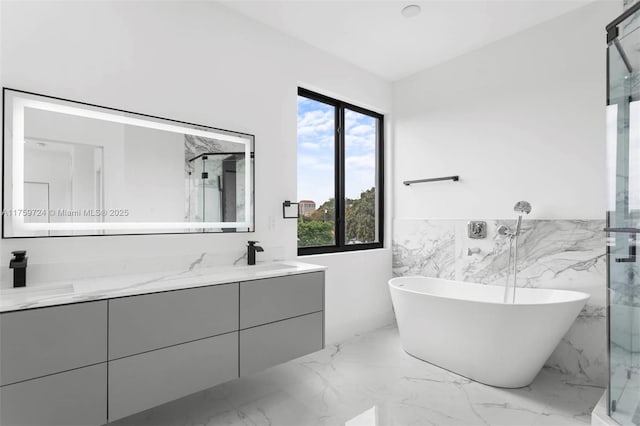 full bathroom featuring double vanity, marble finish floor, a freestanding bath, and a sink