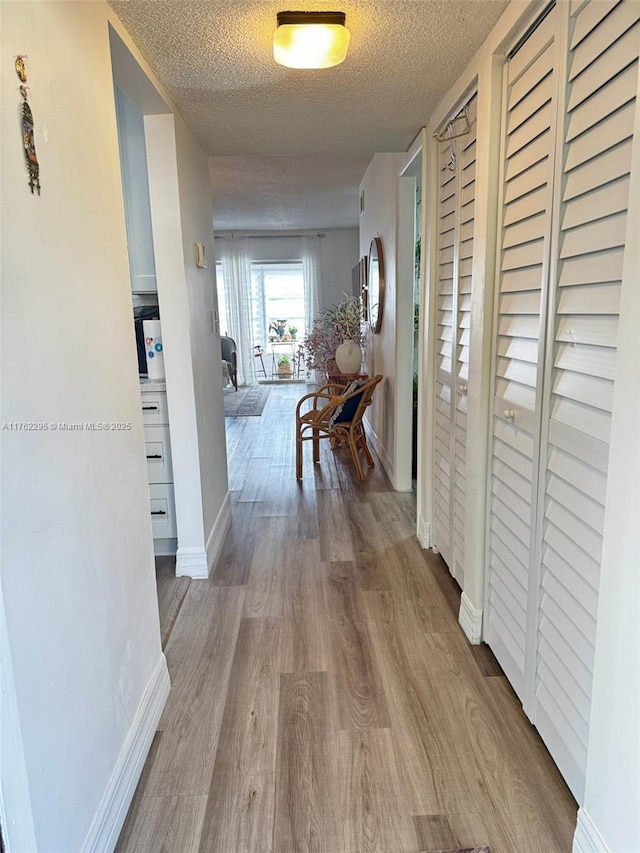 hallway with baseboards, a textured ceiling, and wood finished floors