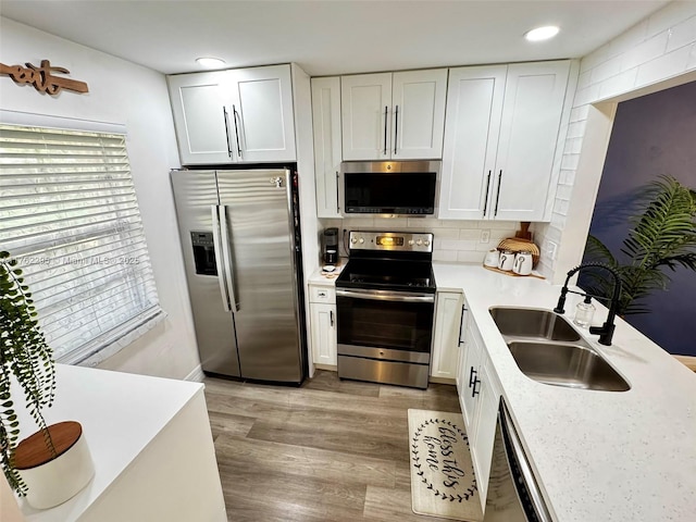 kitchen with light wood-style flooring, a sink, stainless steel appliances, light countertops, and backsplash