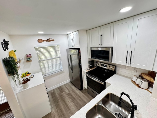 kitchen featuring a sink, light stone counters, wood finished floors, appliances with stainless steel finishes, and white cabinets