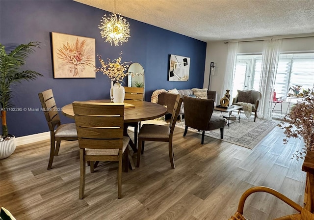 dining space with a notable chandelier, wood finished floors, baseboards, and a textured ceiling