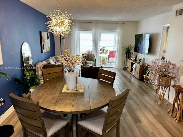 dining area featuring a notable chandelier, a textured ceiling, visible vents, and wood finished floors