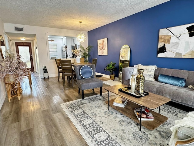 living area with wood finished floors, baseboards, visible vents, a notable chandelier, and a textured ceiling