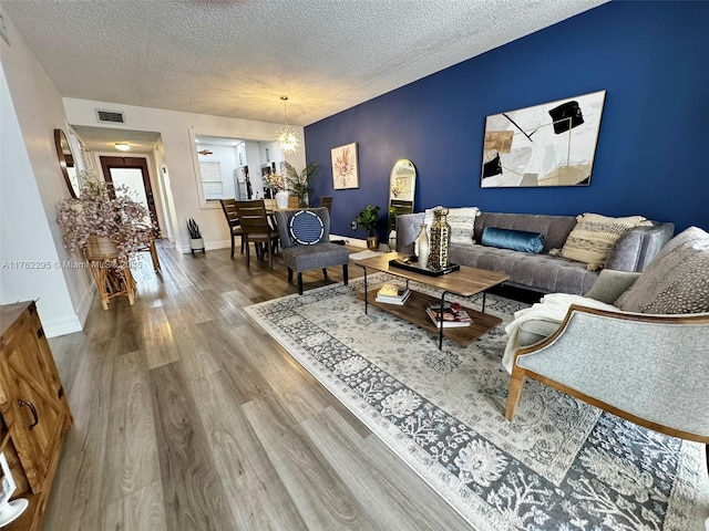 living area with a notable chandelier, visible vents, baseboards, a textured ceiling, and wood finished floors