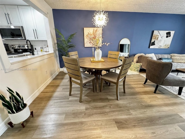 dining area with light wood-style flooring, a textured ceiling, baseboards, and an inviting chandelier