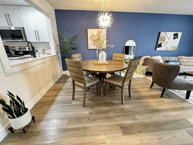 dining space with a textured ceiling, a chandelier, baseboards, and light wood-style floors