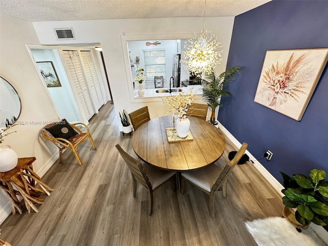 dining room with baseboards, wood finished floors, visible vents, and a textured ceiling