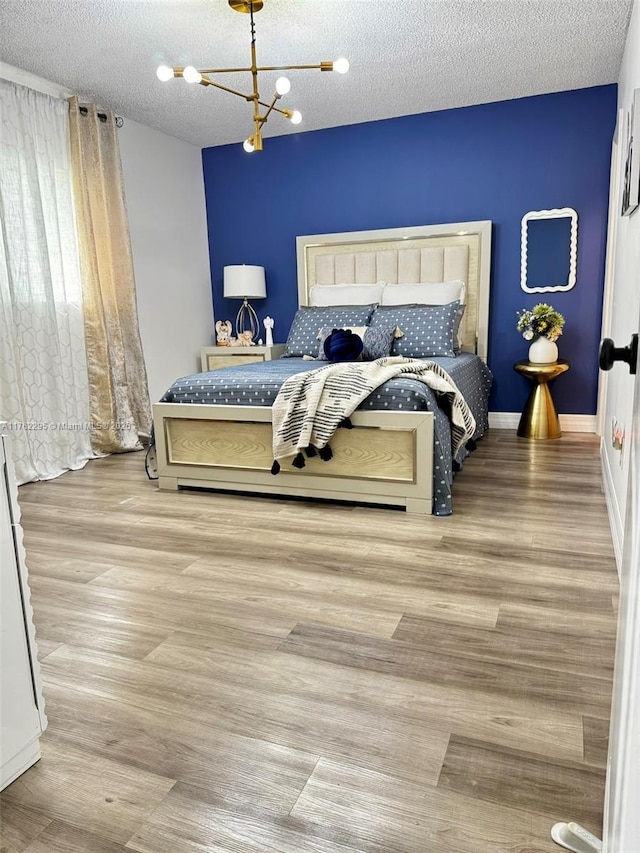 bedroom featuring baseboards, a textured ceiling, an inviting chandelier, and wood finished floors