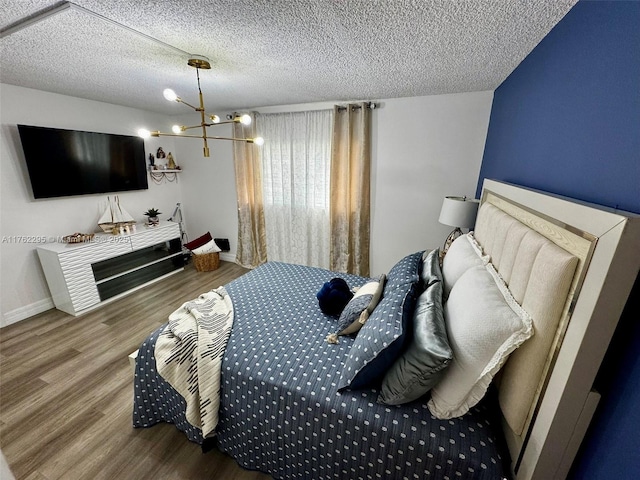 bedroom with a chandelier, a textured ceiling, baseboards, and wood finished floors