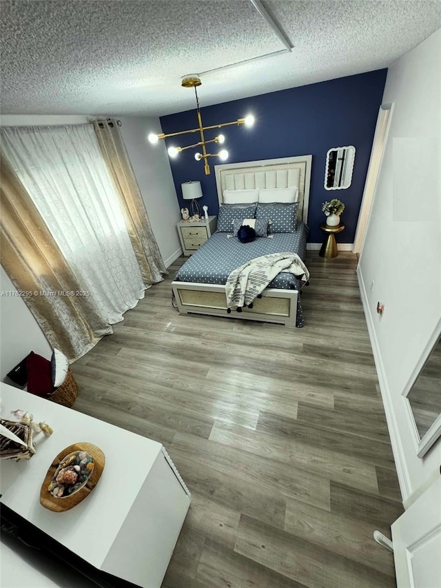 bedroom featuring baseboards, a textured ceiling, an inviting chandelier, and wood finished floors