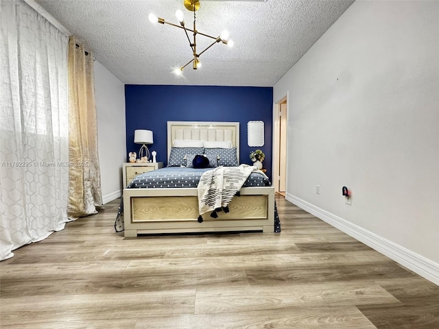 bedroom with a notable chandelier, wood finished floors, baseboards, and a textured ceiling