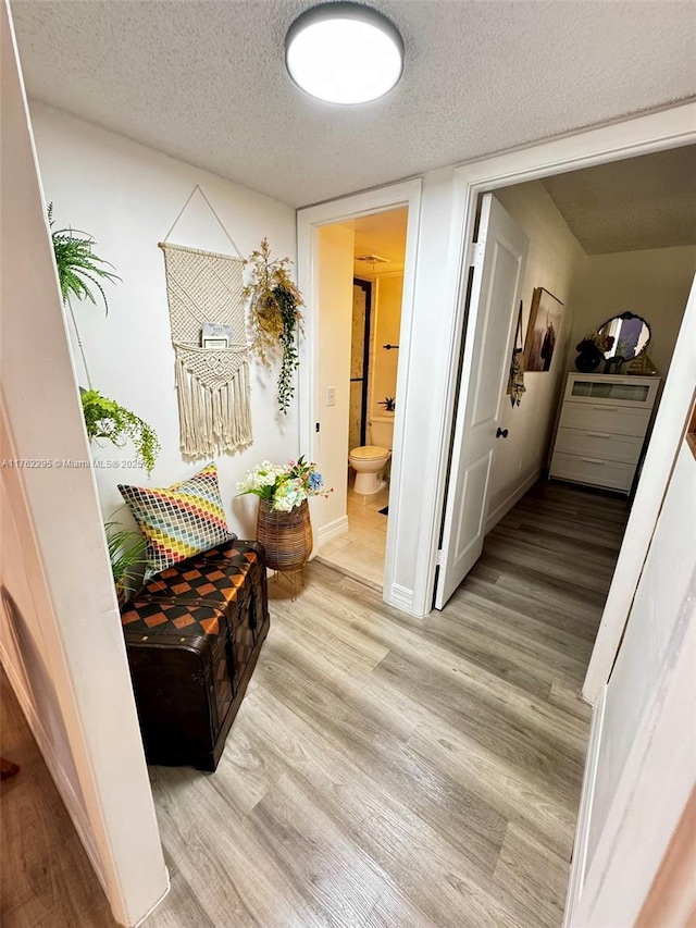 corridor featuring light wood-style flooring, baseboards, and a textured ceiling