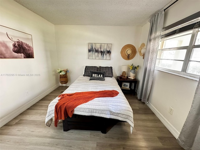 bedroom with a textured ceiling, wood finished floors, and baseboards