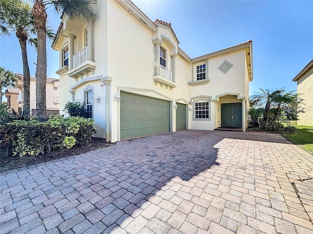 mediterranean / spanish home featuring stucco siding, a tile roof, decorative driveway, and a garage