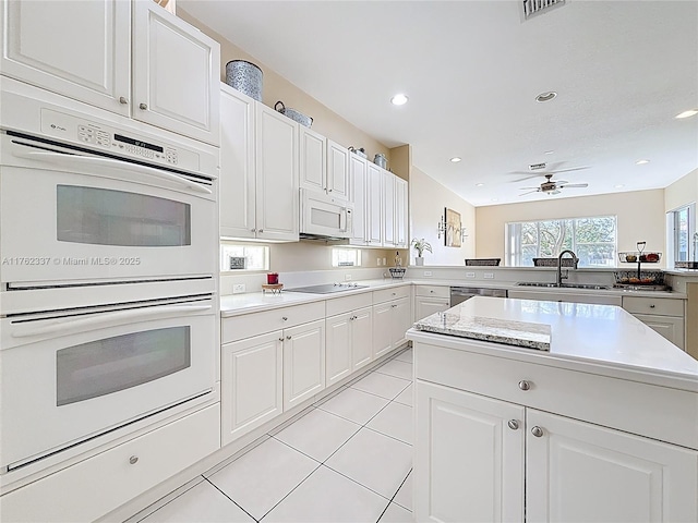 kitchen featuring light countertops, a peninsula, white cabinets, white appliances, and a sink