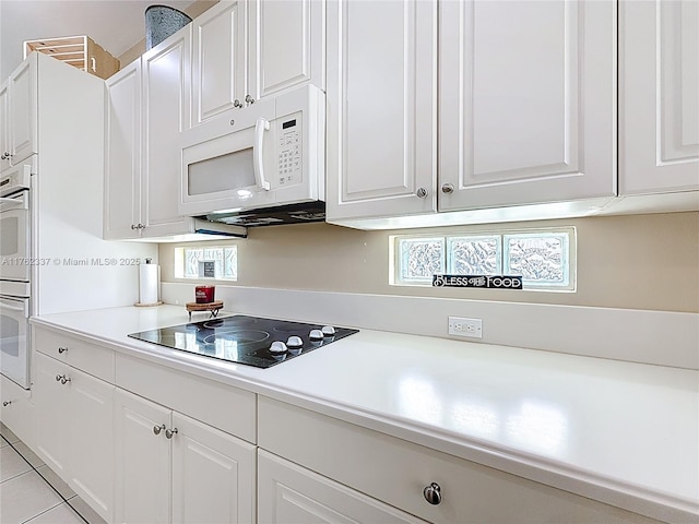 kitchen featuring black electric cooktop, white microwave, white cabinets, and light countertops