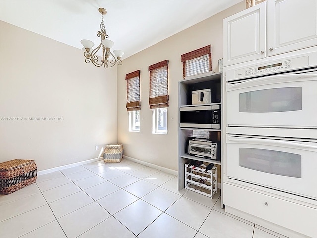 kitchen featuring baseboards, double oven, hanging light fixtures, light tile patterned flooring, and white cabinetry