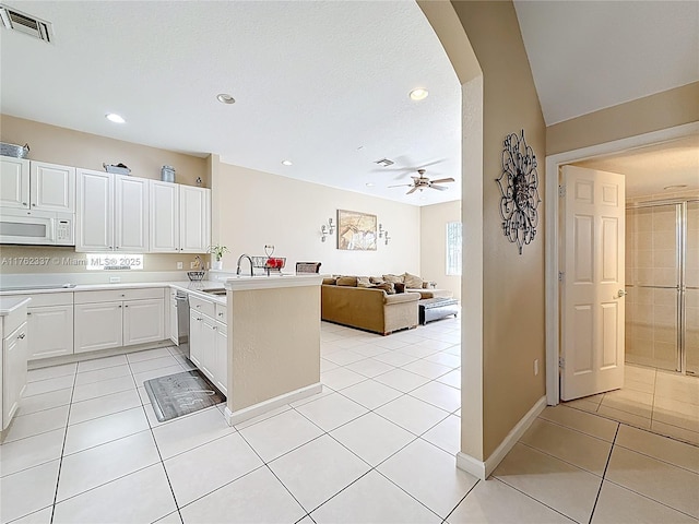 kitchen featuring visible vents, arched walkways, a peninsula, light tile patterned floors, and white microwave