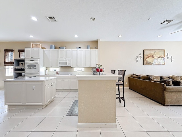 kitchen featuring visible vents, a center island, open floor plan, a kitchen bar, and white appliances