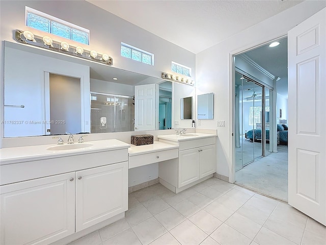 ensuite bathroom featuring tile patterned floors, a stall shower, two vanities, and a sink