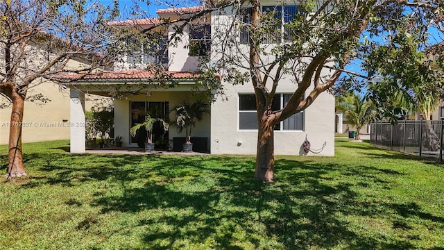 rear view of house featuring a tiled roof, stucco siding, a lawn, and fence