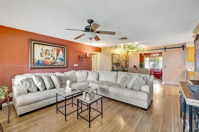 living room with light wood-type flooring, a barn door, visible vents, and ceiling fan