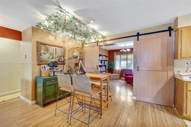 dining room featuring a barn door, baseboards, a textured ceiling, and light wood-style flooring