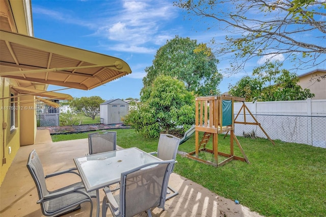 deck featuring a playground, a patio area, a yard, an outbuilding, and a storage unit